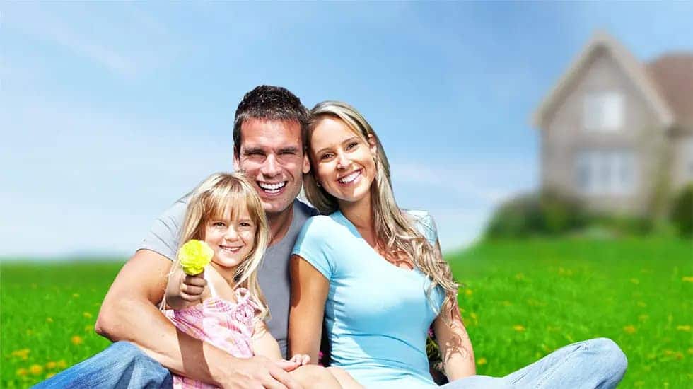 Family Sitting On Grass In Front Of Home